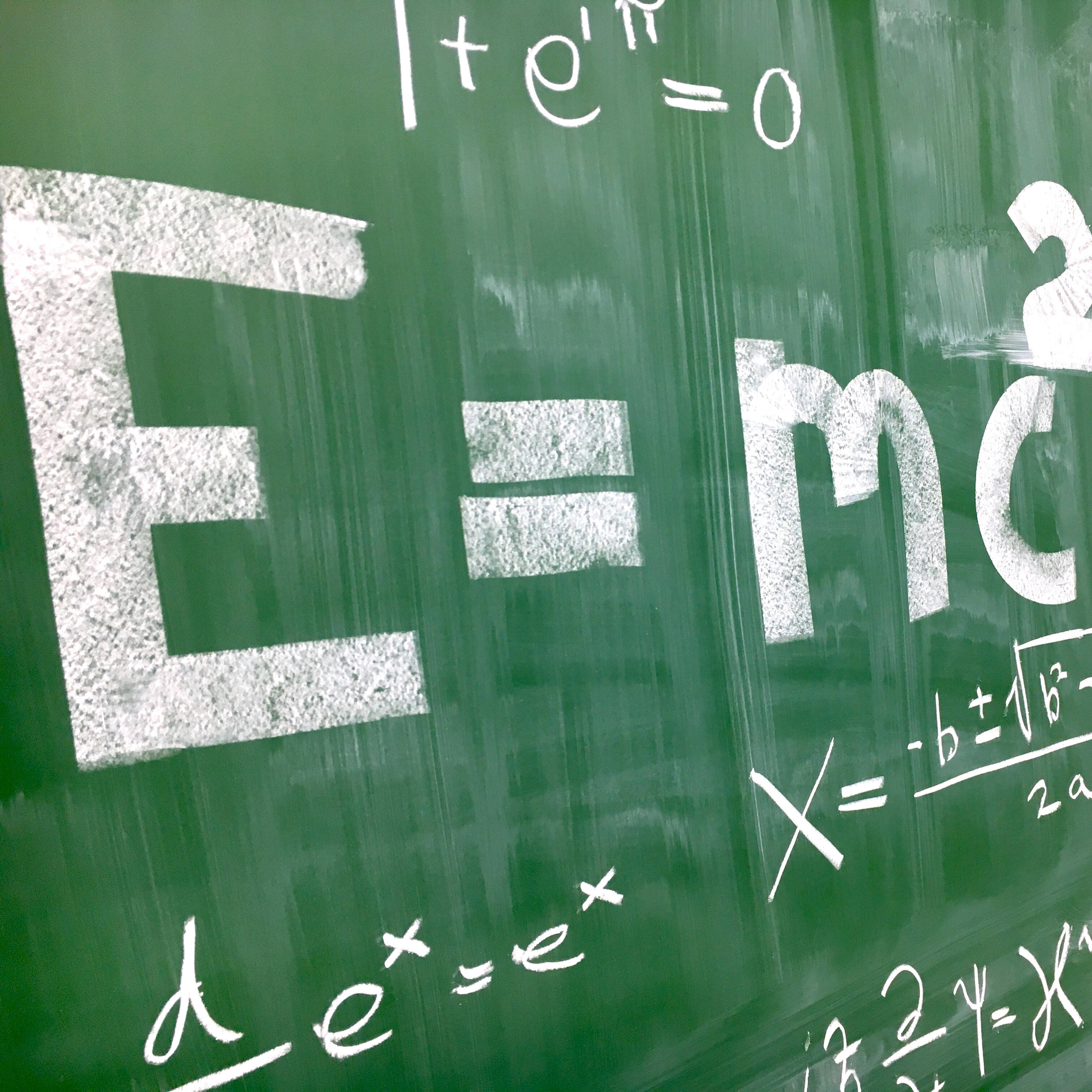 Mathematical equations sprawled across a green board. Einstein's famous equation from special relativity, E=mc^2, most prominently depicted.